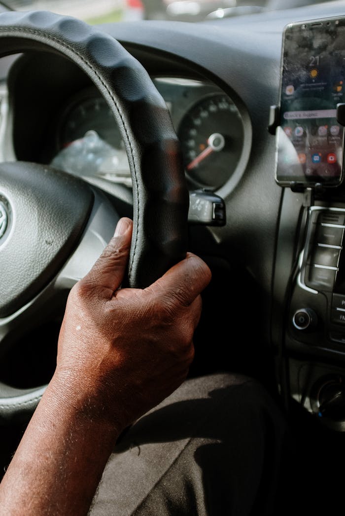 Detailed view of a driver's hand on the steering wheel in a car interior, showcasing dashboard details.